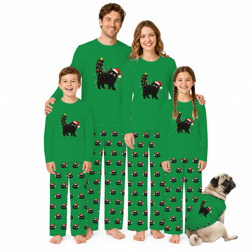 A family of four wearing matching green long-sleeve pajamas with a snowman graphic and white text reading 'Tis the Season Freezin'', standing barefoot against a white background, with a small pug dog wearing a matching pajama set beside them.