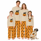 A family of four wearing matching Beige long-sleeve pajamas with orange Halloween-themed graphics, standing barefoot on a White background, with a small dog sitting beside them wearing a matching pajama set.