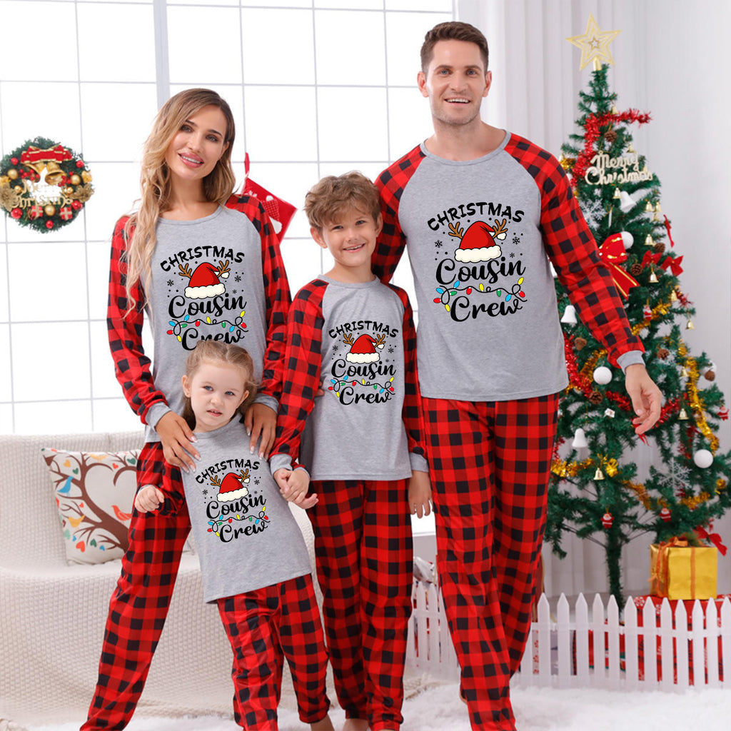 A family of four wearing matching red and black plaid and gray raglan Christmas pajamas with a 'Gnomies' graphic, posed in a festive living room with a decorated Christmas tree and wreath.