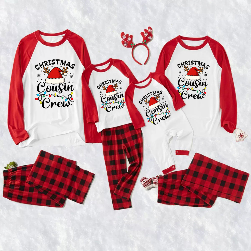 A family matching Christmas cousin crew pajama set laid out on a white textured background, including long-sleeve raglan shirts and plaid pants in red and black, plus a red reindeer antler headband.