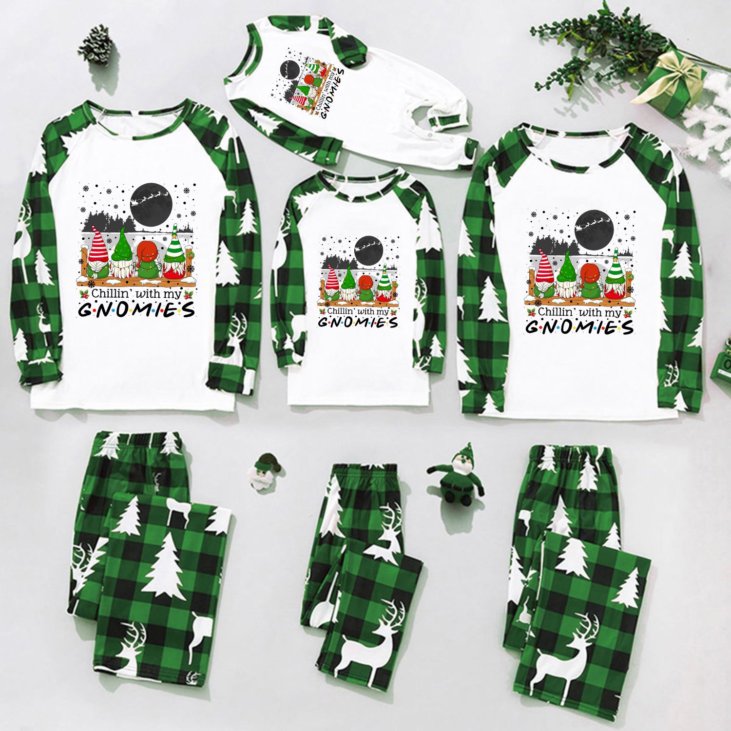 A coordinated family pajama set laid out on a white background, including long-sleeve raglan shirts and matching pants in green plaid and green-and-white animal print, with Christmas gnome graphics and holiday decorations.