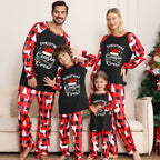 A family of four wearing matching Christmas-themed long-sleeve pajamas, standing together in front of a beige couch with a decorated Christmas tree on the right. The pajamas feature a black front with white text reading 'Christmas Cousin/Crew' and a red-and-white buffalo plaid pattern on the sleeves and pants, with white reindeer prints.