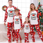 A family of four wearing matching Christmas-themed pajamas with the text 'Christmas Cousin/Cousin Crew' on the front, posed in a festive living room with a decorated Christmas tree and holiday wreath.