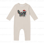 A long-sleeve baby romper in a light oatmeal beige color, featuring a graphic of a raccoon wearing a Santa hat and wrapped in Christmas lights on the chest. The romper has snap closures at the crotch.