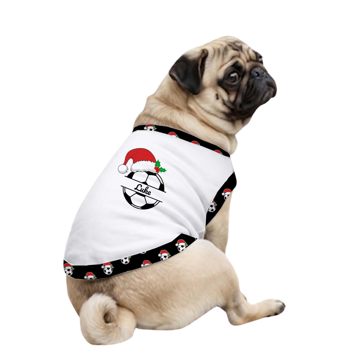 A fawn pug dog wearing a white pet shirt with a black patterned trim. The shirt features a soccer ball graphic decorated with a red Santa hat, green holly leaves, and the name 'Dane' in script across the center.