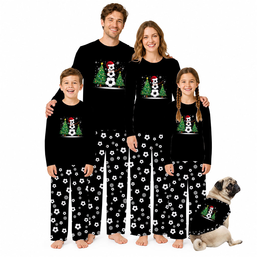 A family of four wearing matching black long-sleeve pajamas with a Christmas snowman graphic on the chest and white soccer-ball patterned pants, standing against a white background. A small pug dog sits at the bottom right wearing a matching pajama set.