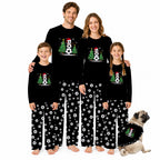 A family of four wearing matching black long-sleeve pajamas with a Christmas snowman graphic on the chest and white soccer-ball patterned pants, standing against a white background. A small pug dog sits at the bottom right wearing a matching pajama set.