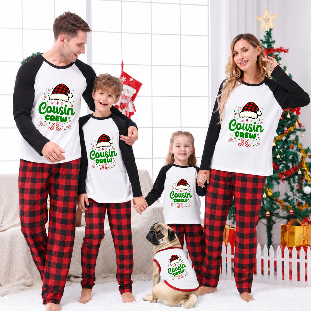 A family of four and a dog wearing matching holiday cousin-themed pajamas, standing in a living room with a Christmas tree, stockings, and wrapped gifts in the background.