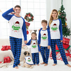 A family of four and a dog wearing matching blue and white long-sleeve pajamas with a 'Cousin Crew' holiday graphic, standing in a festive living room with a Christmas tree, wreath, and wrapped gifts.