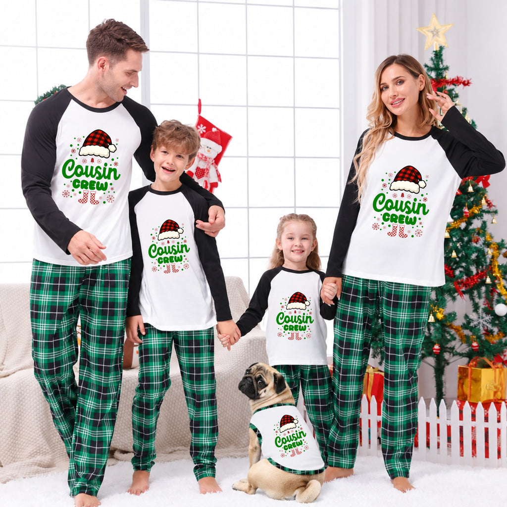 A family of four and a dog wearing matching Christmas raglan pajamas in a decorated living room. The matching set features white long-sleeve tops with black sleeves and green plaid pants