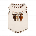 A sleeveless Cream-coloRed pet shirt featuring a graphic of three Highland cows under Christmas lights, with a small brown cow pattern printed around the neckline and hem.