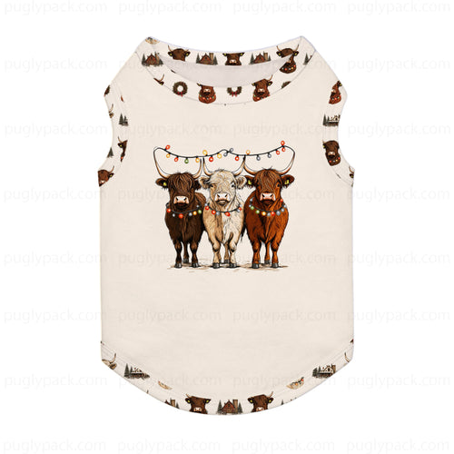 A sleeveless Cream-coloRed pet shirt featuring a graphic of three Highland cows under Christmas lights, with a small brown cow pattern printed around the neckline and hem.