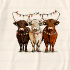 A graphic print on a Cream-coloRed fabric featuring three Highland cows wearing colorful Christmas string lights. The background has a repeating watermark of 'puglypack.