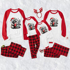 Three matching family Christmas pajama sets laid out on a white textured background, including long-sleeve raglan tops with red sleeves and a raccoon graphic that reads 'Cute But Feral,' red-and-black plaid pants, and a red reindeer antler headband.