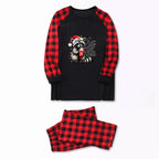 A two-piece holiday pajama set featuring a long-sleeve top and matching pants. The top is black with red and black buffalo plaid raglan sleeves and a front graphic of a raccoon wearing a Santa hat with the text 'Cute but Feral'.