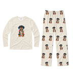 A two-piece pajama set on a plain White background, featuring a Cream long-sleeve shirt with a colorful dachshund graphic on the chest and matching Cream pants with an all-over dachshund print.