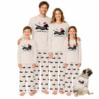 A family of four and a dog wearing matching holiday-themed long-sleeve pajamas with a Black silhouette graphic, Red Santa hat, and 'Through the Snow' text, posed against a plain White background.