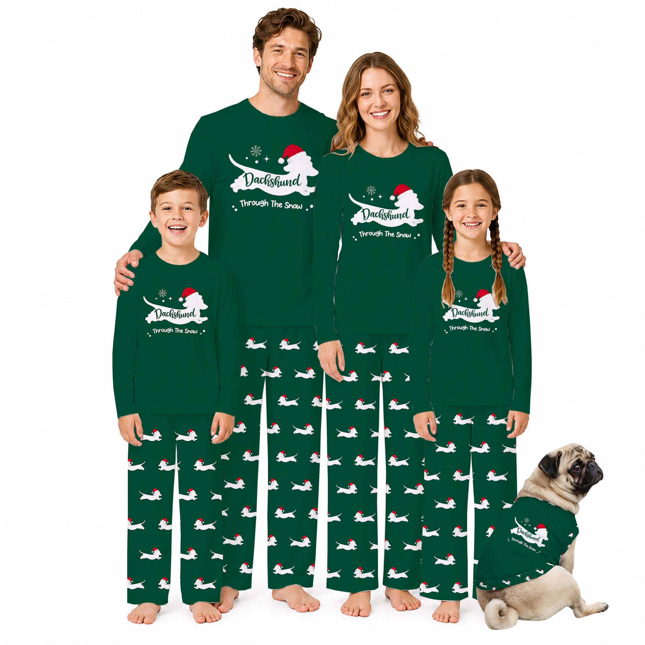 A family of four wearing matching dark Green Christmas-themed long-sleeve pajamas with a White dog graphic and 'Through the Snow' text, standing barefoot against a White background. A small pug dog sits at their right, wearing a matching pajama set.