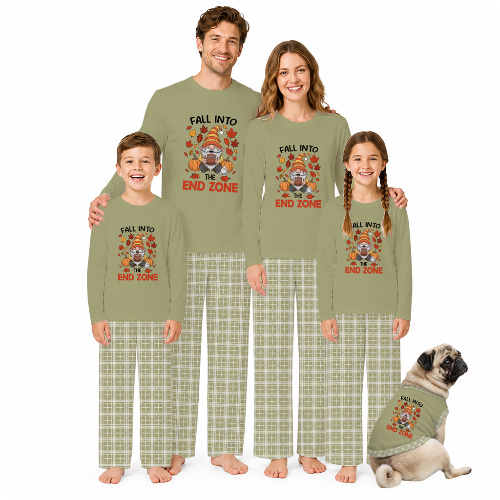 A family of four wearing matching sage green Thanksgiving-themed pajamas with a turkey graphic and plaid pants, standing barefoot on a white background next to a small matching dog.