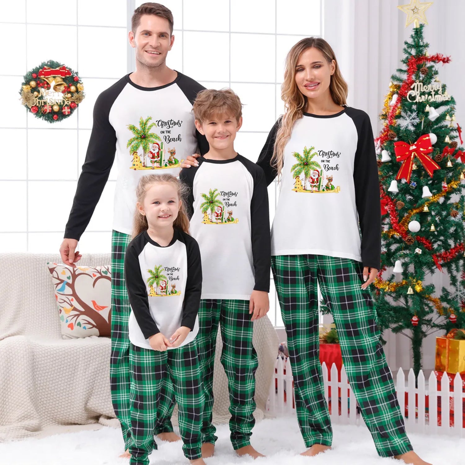 A family of four wearing matching Christmas-themed raglan pajamas stands together in a decorated living room. The pajama set has a White front with Black sleeves and a colorful tropical Santa graphic, paiRed with Green plaid pants.