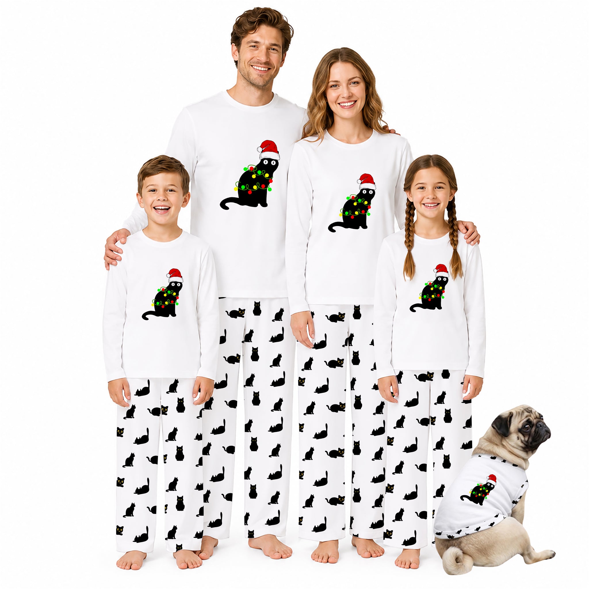 A family of four wearing matching white long-sleeve pajamas with a black cat print and Santa hat graphic, standing barefoot against a white background, with a small dog sitting at their feet wearing a matching pajama set.