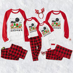 A family matching holiday pajama set laid out on a white textured background, including three long-sleeve raglan tops with red sleeves and red gnomes graphics, three matching pants in red buffalo plaid, a red reindeer antler headband, and small red-and-white booties. The tops read 'Cabin with my GNOMIES' and the pants say 'ALL IN A RED AND BLACK BUFFALO PLaid'.