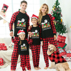 A family of four wearing matching black and red plaid Christmas pajamas with a 'Gnomes' graphic on the front, posed in a living room with a Christmas tree, wrapped gifts, and a golden retriever dog wearing a matching pajama shirt.