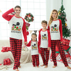 A family of four wearing matching Christmas-themed long-sleeve pajamas stands together in a decorated living room. The pajamas have red and black buffalo plaid legs with white fronts and red sleeves, featuring a festive Santa graphic.