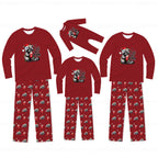 Three sizes of matching Christmas family pajamas shown on a white background, including long-sleeve shirts and pants. The pajamas are red with a raccoon wearing a Santa hat graphic on the chest and red pants featuring a repeating pattern of the same raccoon design.
