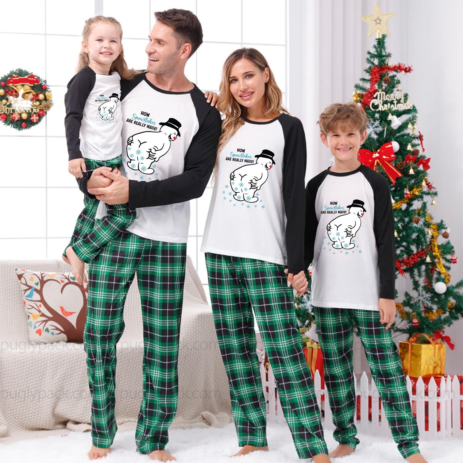 A family of four wearing matching Christmas pajamas, including a dad, mom, and two children, standing together in a festive living room with a decorated Christmas tree and wreath.