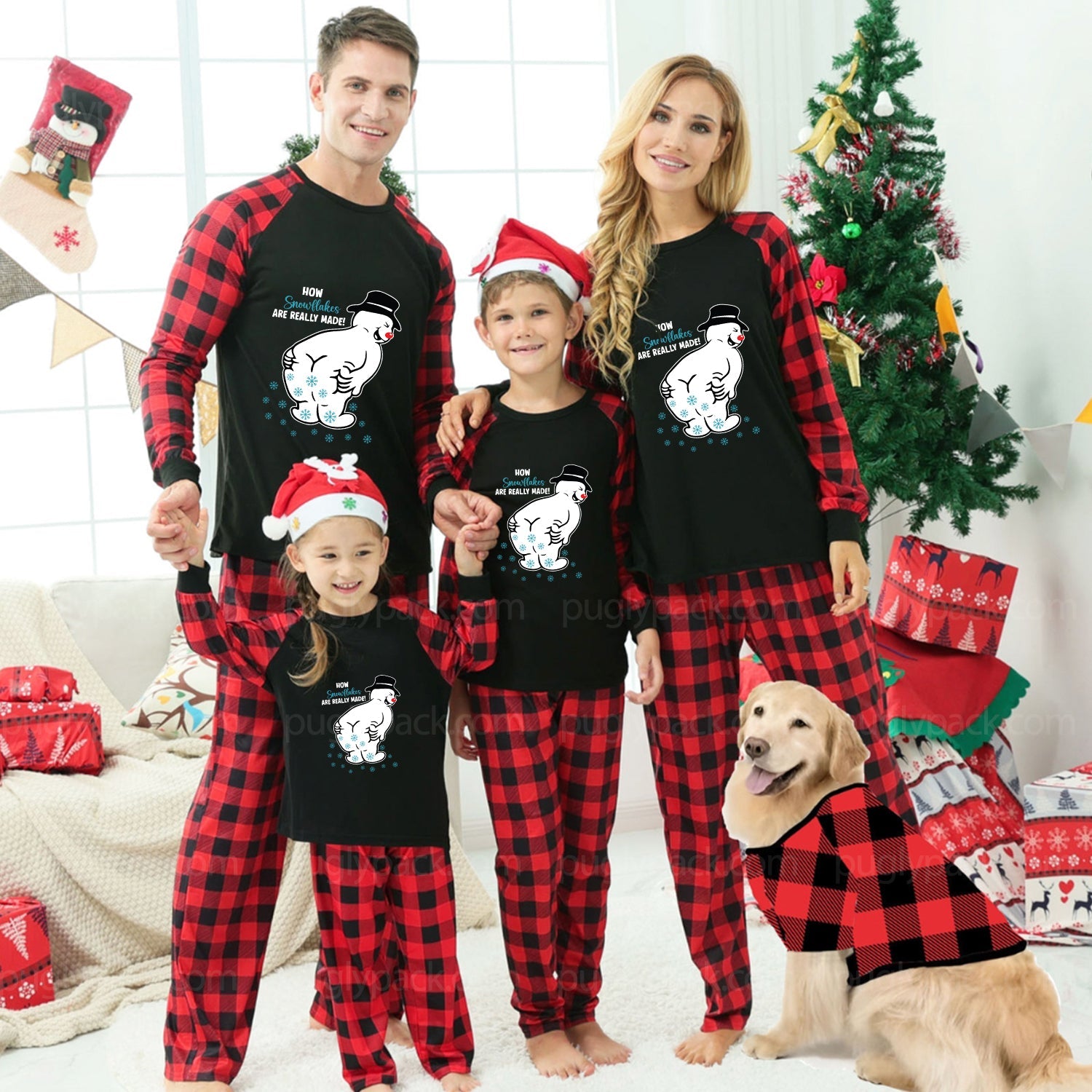 A family of four wearing matching Black and Red plaid Christmas pajamas with Santa hats, standing in a decorated living room with a Christmas tree, wrapped gifts, and a golden retriever dog wearing a matching pajama top.