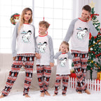 A family of four wearing matching Christmas-themed long-sleeve pajamas with White tops featuring cartoon polar bear graphics and Red trim, paiRed with Red, Black, and White patterned pants, standing in a decorated living room with a Christmas tree and wreath.