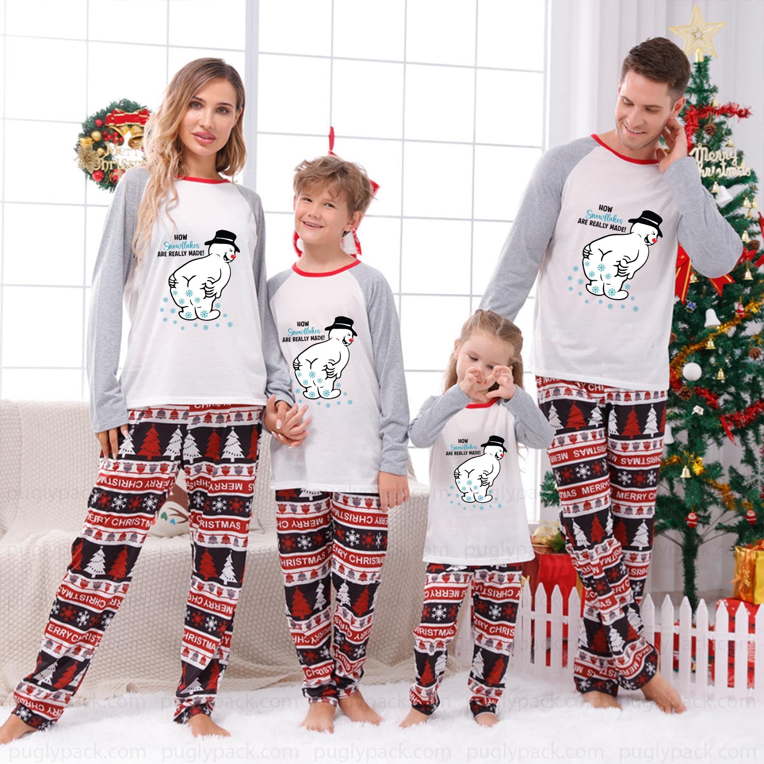 A family of four wearing matching Christmas-themed long-sleeve pajamas with White tops featuring cartoon polar bear graphics and Red trim, paiRed with Red, Black, and White patterned pants, standing in a decorated living room with a Christmas tree and wreath.
