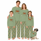 A family of four wearing matching sage green long-sleeve pajamas with a brown bear graphic on the chest and green cactus-print pants, standing together on a white background with a small pug dog wearing a matching pajama set.