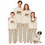 A family of four wearing matching long-sleeve pajamas with a cowboy and cow print, standing together on a white background with a small dog wearing a matching pajama shirt.