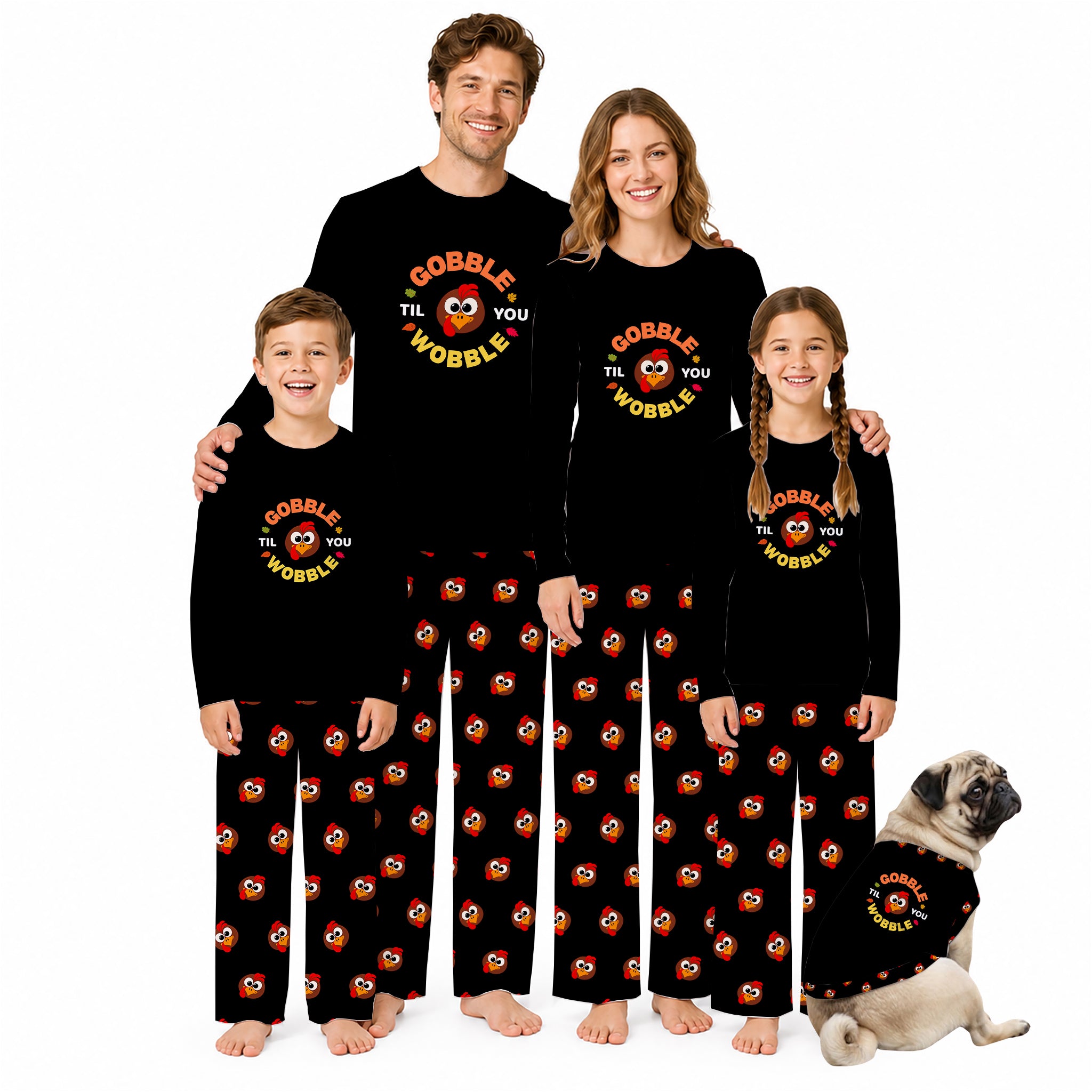 A family of four wearing matching Black long-sleeve pajamas with a colorful 'Gobble the Wobble' cartoon graphic on the chest and Red, orange, and yellow patterned pants, posed with a small matching dog on a White background.
