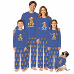 A family of four and a pug dog wearing matching royal Blue pajamas with a repeating gingerbread cookie pattern and a Santa Claus dog graphic on the chest. The pajamas have 'Feliz Navidad' printed below the graphic.