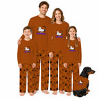 A family of four and a dog wearing matching Halloween-themed long-sleeve pajamas. The pajamas are rust brown with Black and orange pumpkin and bat patterns, and feature a White dachshund graphic with Purple 'Halloween Dog' text.