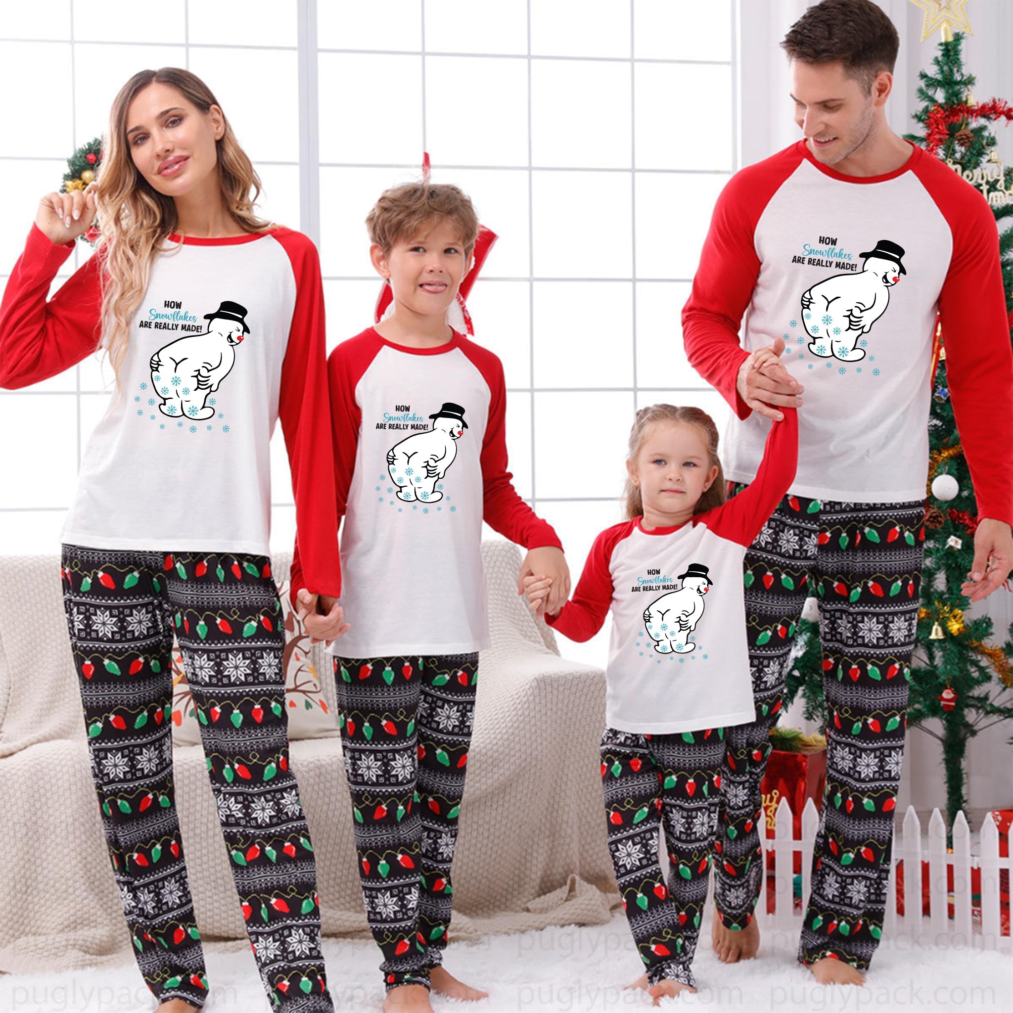 A family of four wearing matching Christmas pajamas, standing in a decorated living room with a Christmas tree and window in the background. The pajamas feature a White and Red raglan top with a cartoon polar bear graphic, paiRed with Black patterned pants decorated with holiday motifs.