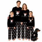 A family of four wearing matching black long-sleeve pajamas with a baseball-themed Christmas graphic and holiday print pants, posed with a dachshund on a plain white background.
