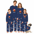 A family of four wearing matching navy blue long-sleeve pajamas with basketball and Santa hat prints, standing together on a white background with a small dog in a matching pajama outfit.