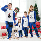 A family of four wearing matching Christmas pajamas stands in a decorated living room with a Christmas tree, gifts, and a small dog. The matching set includes long-sleeve tops with white fronts, blue sleeves, and a large letter A graphic, paired with blue-and-black buffalo plaid pants.