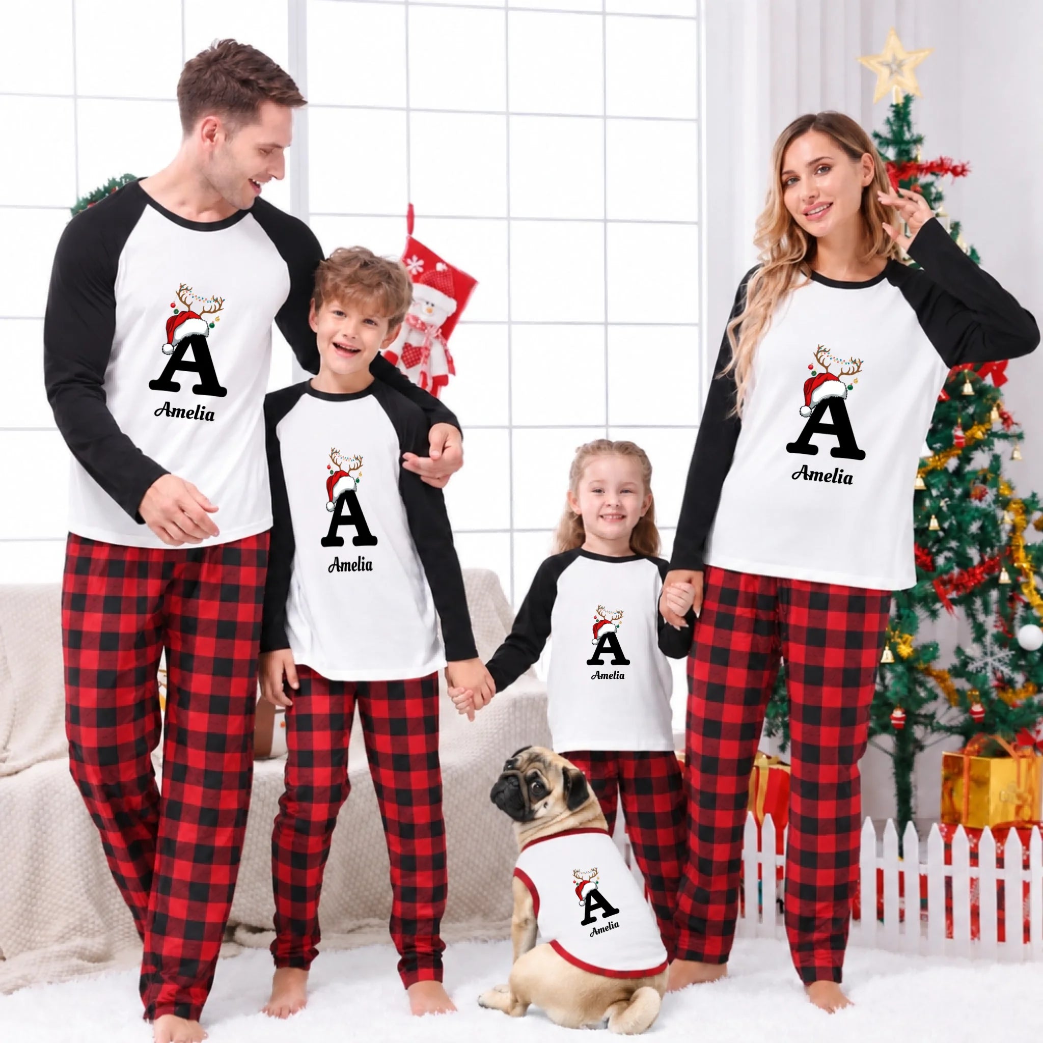 A family of four and their dog wearing matching Christmas pajamas with a white front, black long sleeves, and red plaid pants, standing in a decorated living room with a Christmas tree and stockings.