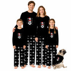 A family of five wearing matching black long-sleeve pajamas with a white snowman graphic on the chest and a white snowman pattern on the pants, standing together on a white background with a small pug dog wearing a matching pajama shirt.