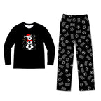A two-piece kids' pajama set on a plain white background. The long-sleeve shirt is black with a festive graphic of a snowman wearing a red Santa hat and scarf next to a soccer ball.