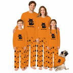 A family of four and a dog wearing matching orange Halloween pajamas with a black cat graphic and 'Spooky Baby' text, posed against a plain white background.