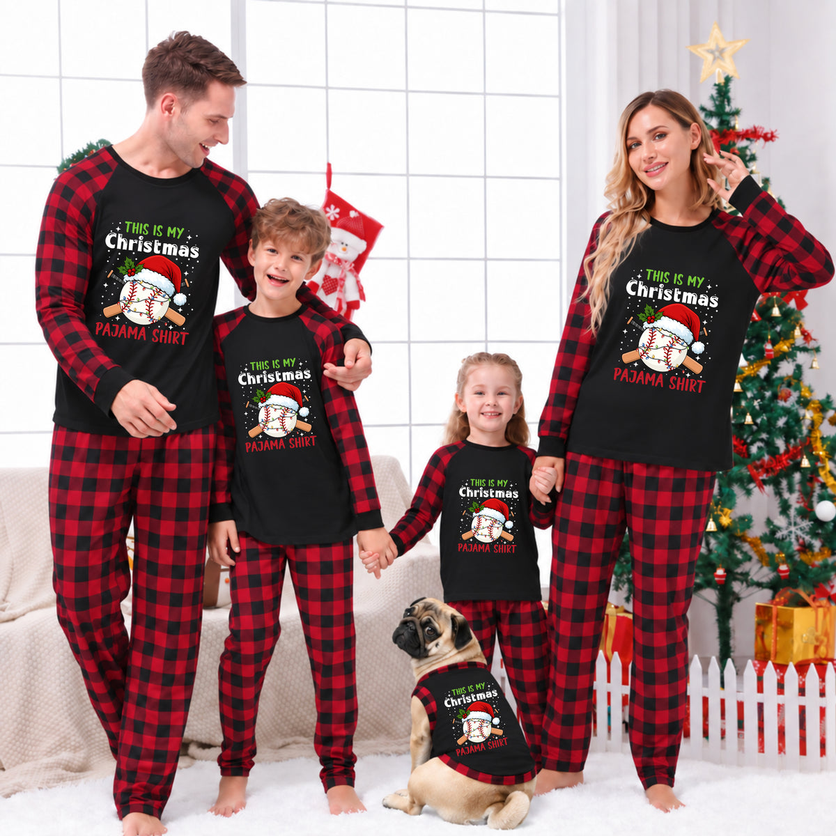 A family of four and a dog wearing matching red and black plaid Christmas pajamas with a black chest graphic that reads 'THIS IS MY Christmas PANDA SHIRT' in festive lettering. The background shows a decorated Christmas tree, stockings, and a cozy indoor holiday setting.
