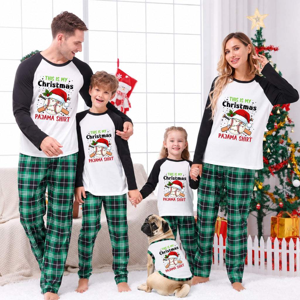 A family of four and a dog wearing matching Christmas pajamas in a festive living room. The matching set features a white long-sleeve top with black sleeves and a festive graphic that reads 'THIS IS MY Christmas PAMMA SHIRT' with a Santa bear, paired with green and black plaid pajama pants.