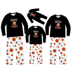 Three matching Christmas-themed long-sleeve pajama sets for different sizes, displayed on a solid white background. Each set features a black crewneck shirt with a festive graphic and white pants patterned with orange basketballs, gray snowflakes, and small red accents.