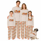 Four people and a small dog wearing matching Beige long-sleeve pajamas with a 'YES THE SEASON' autumn sports print and patterned pants, posed together on a White background.